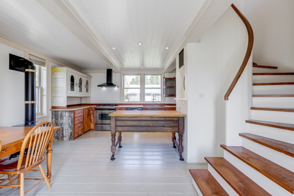 Bright kitchen interior featuring a wooden dining table, stove, and a staircase.